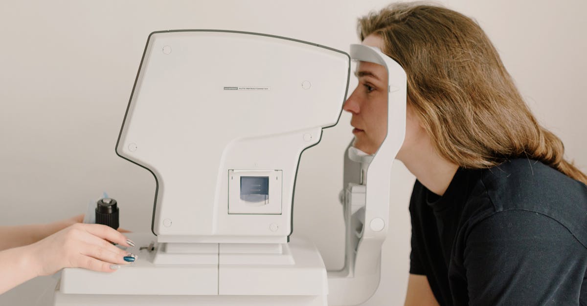 Side view of crop anonymous doctor checking eyesight of female patient using vision screening device in clinic
